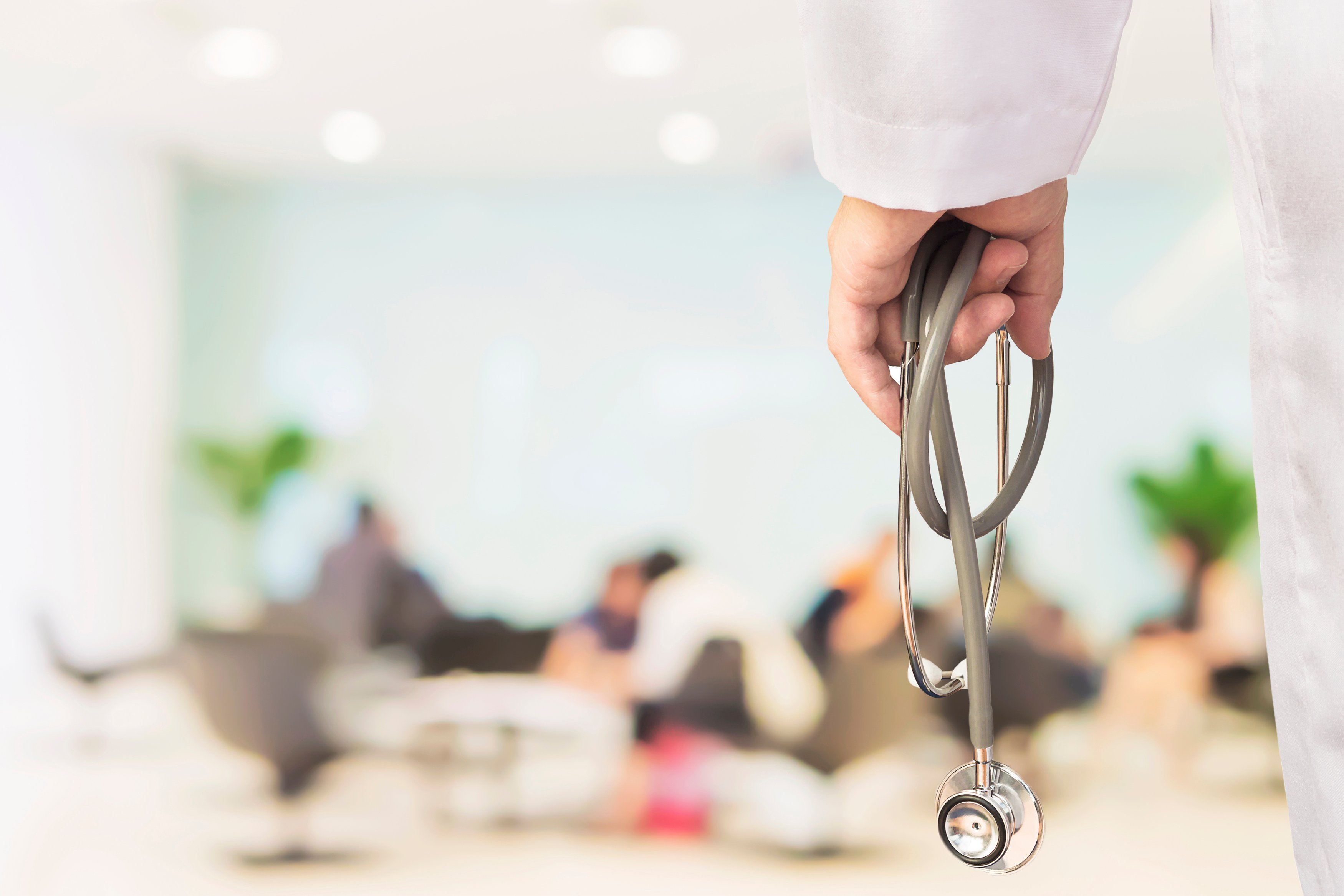 OBGYN doctor holding a stethoscope with patients waiting in the background, symbolizing how medical website development for OBGYNs helps independent practices compete and win against hospitals.