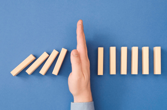 Hand stopping a row of falling dominoes, symbolizing how proactive fact management in healthcare SEO prevents small errors from causing bigger problems.