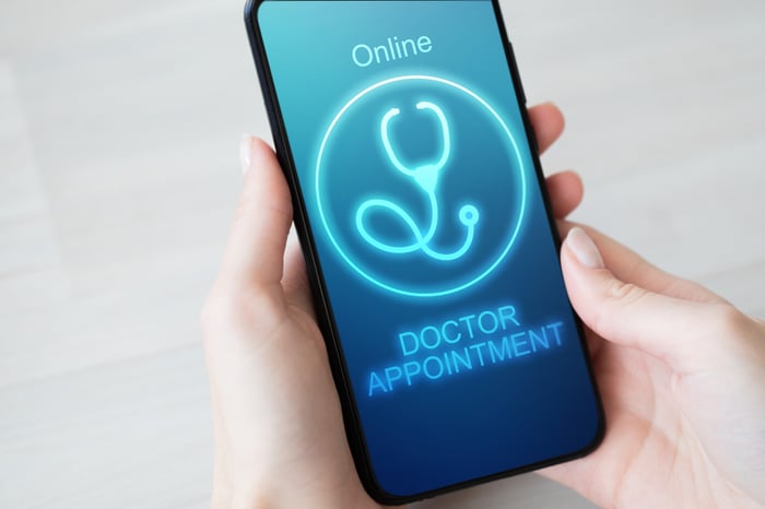 Patient holding a smartphone showing an online doctor appointment booking screen – symbolizing seamless digital patient engagement with PracticeBeat.