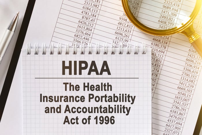 HIPAA compliance analysis concept with financial reports, red pen, and magnifying glass on table—symbolizing risk evaluation in healthcare market.
