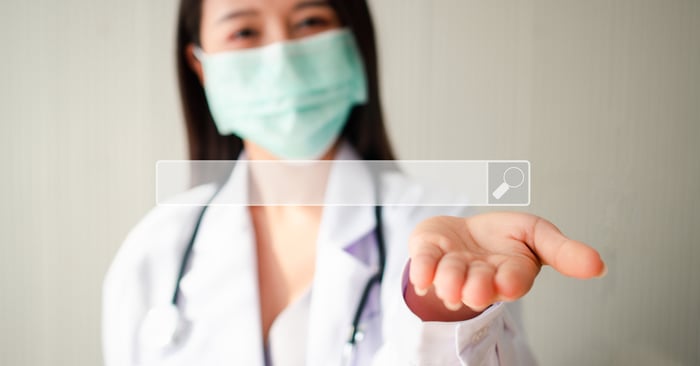Female doctor in a mask extending her hand with a virtual search bar overlay — symbolizing how PracticeBeat helps private practices get discovered by patients online.