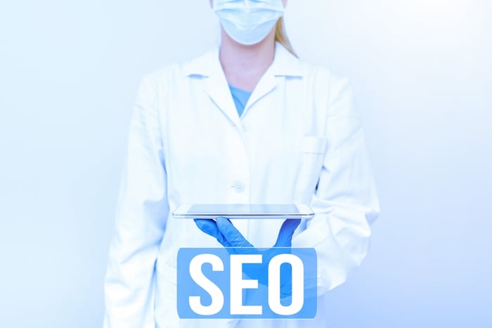 A lady doctor holding a tablet with SEO text, symbolizing the importance of SEO for medical practices to attract patients online