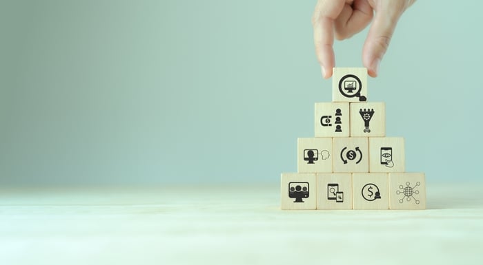 Hand placing the final block on a pyramid of marketing strategy icons, symbolizing measuring and refining the remaining 80% of digital marketing efforts for doctors.