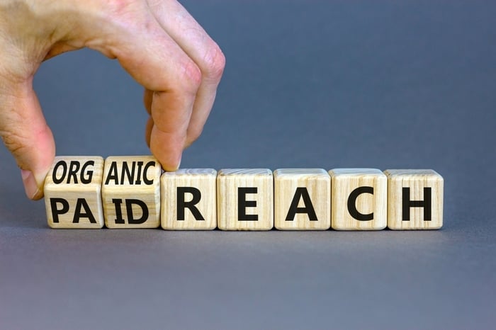 "Hand flipping wooden blocks between 'PAID' and 'ORGANIC' to spell 'REACH,' symbolizing the balance between paid ads and organic SEO in digital marketing."