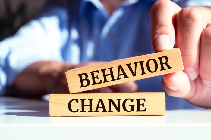 Close-up of a person holding wooden blocks spelling 'Behaviour Change', symbolizing shifting patient behavior in the digital healthcare landscape.
