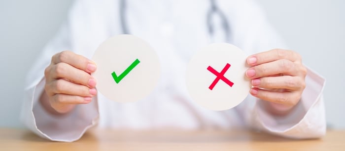 Doctor holding up green checkmark and red cross signs, symbolizing right and wrong strategies—highlighting the 7 digital marketing mistakes private practices must avoid.