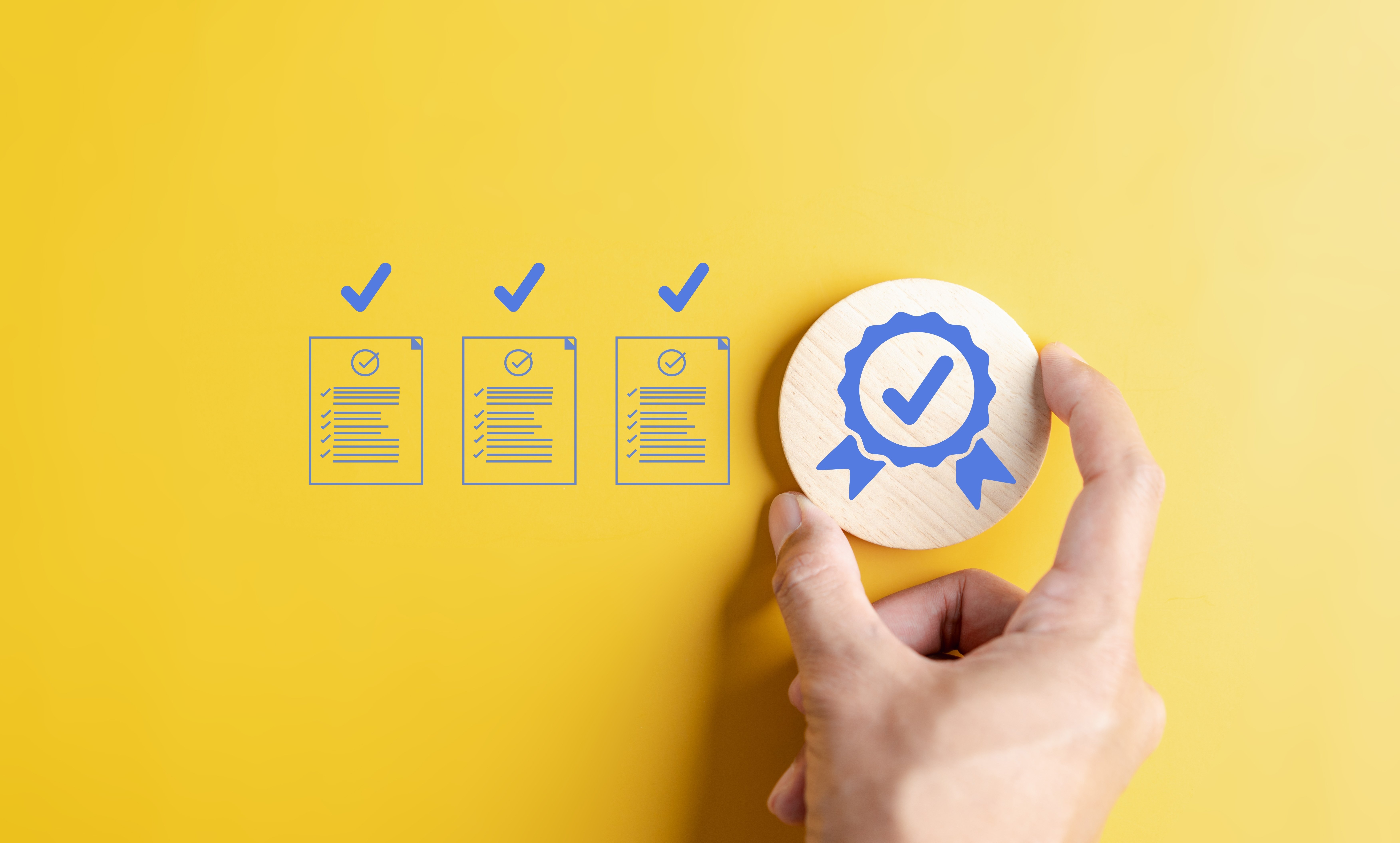 Hand holding a wooden badge with a checkmark beside documents marked with blue check icons, symbolizing verified compliance and quality assurance in medical website development.