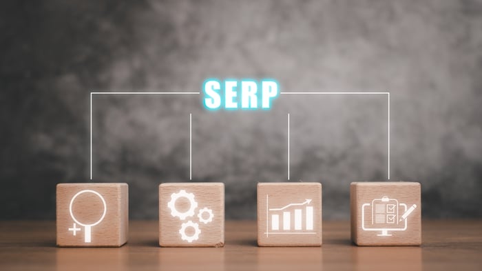 A conceptual diagram illustrating the four pillars of a modern search result. The word 'SERP' is shown in glowing blue text, with lines connecting it to four wooden blocks featuring white icons: a magnifying glass for search, gears for technical optimization, a rising bar chart for growth, and a digital clipboard for structured data and results.