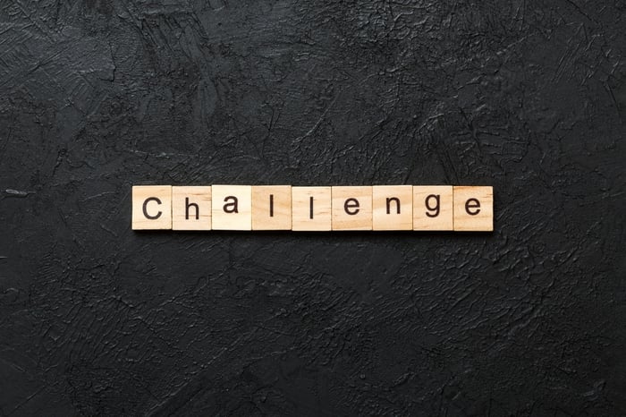 A dark, textured background with wooden tiles spelling "Challenge," representing the obstacles an independent doctor faces when exiting a hospital system to build a $2M growth engine with a healthcare SEO agency.