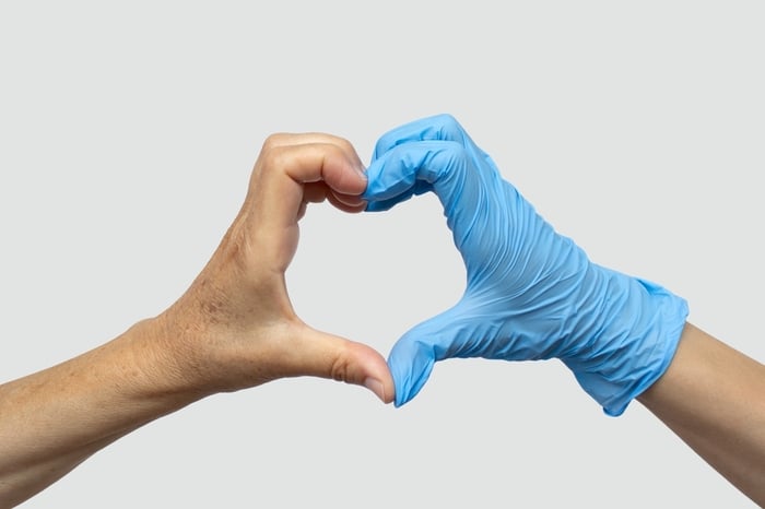 Close-up of two hands forming a heart shape—one bare representing patients, and one wearing a blue medical glove representing healthcare providers—symbolizing the trusted partnership between PracticeBeat and care providers.