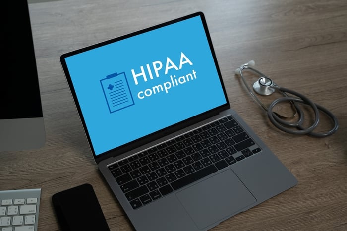 Laptop screen displaying 'HIPAA compliant' with medical clipboard icon, symbolizing data privacy standards for medical websites, alongside a stethoscope on a wooden desk.