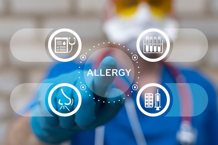 Healthcare professional wearing gloves and protective gear pointing at a digital interface displaying the word ‘Allergy’ surrounded by medical allergy-related icons