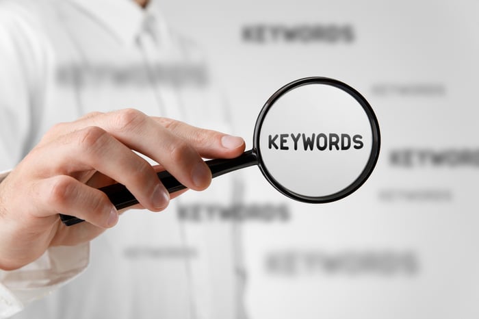 Hand holding a magnifying glass focusing on the word “KEYWORDS,” representing the evolving role of keywords in modern SEO and AI-driven search strategies.
