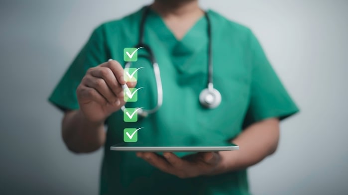 Doctor in green scrubs using a tablet with a checklist of green tick marks — symbolizing the essential steps to strengthen E-E-A-T (Experience, Expertise, Authoritativeness, Trustworthiness) in a medical SEO strategy.