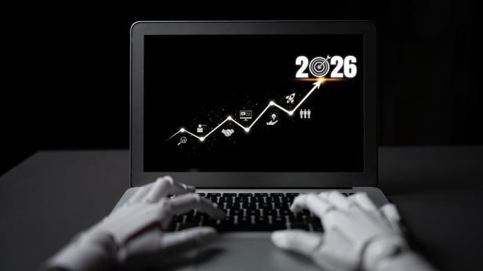 Robot hands typing on a laptop keyboard. The screen displays a digital growth graph rising toward a target bullseye marked '2026', symbolizing automated, forward-looking digital marketing strategy execution for doctors to achieve 2026 goals with PracticeBeat.