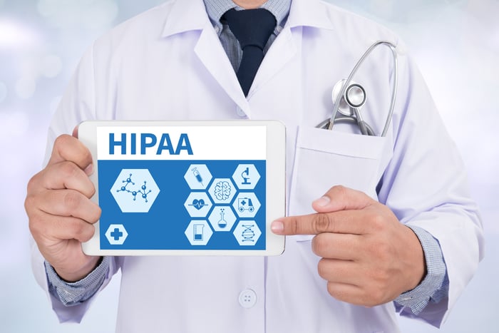 Doctor holding tablet displaying HIPAA compliance icons representing patient data privacy and security in medical website development.