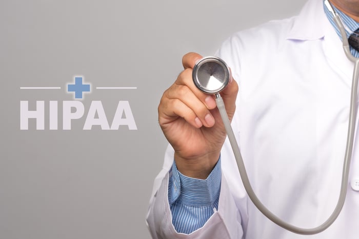 Doctor in white coat holding a stethoscope with the word 'HIPAA' and a medical cross symbol, representing HIPAA-compliant medical website development and patient data privacy.