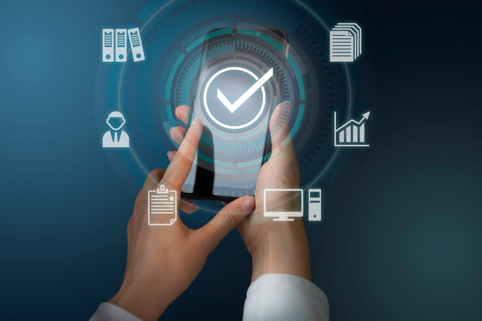Hands using a smartphone with digital icons for data management, analytics, and compliance, representing how PracticeBeat helps healthcare providers manage digital facts smarter and build patient trust.